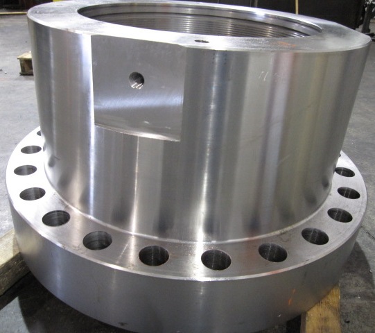 Large machined body flange with threaded bore, hub and drilled bolt holes on the shop floor